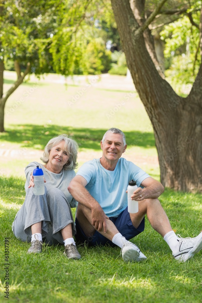 Fototapeta premium Mature couple sitting with water bottles at park