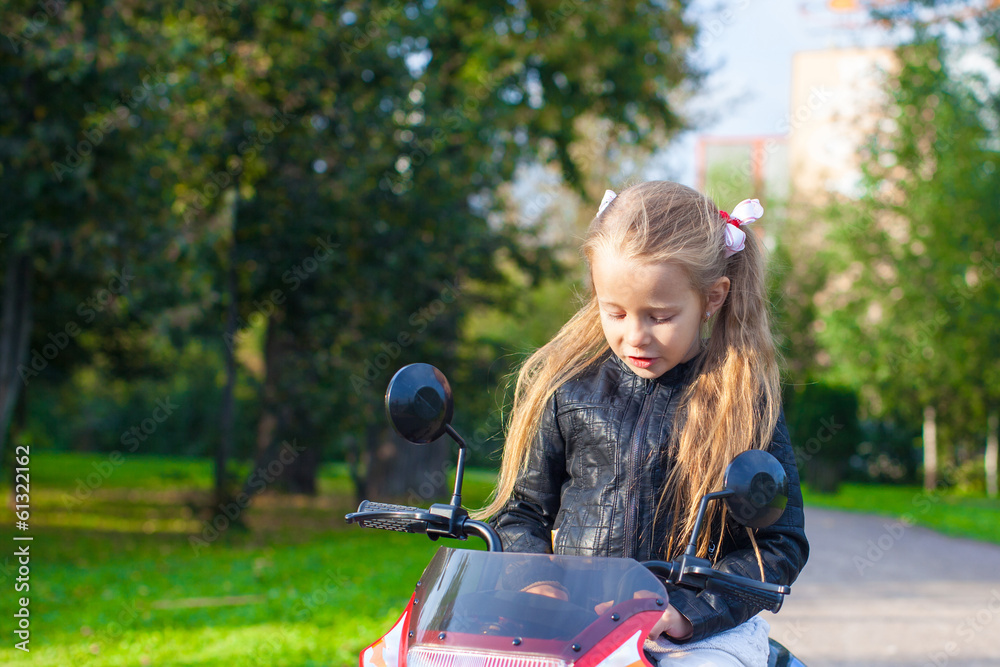 Adorable happy little girl in leather jacket sitting on her toy
