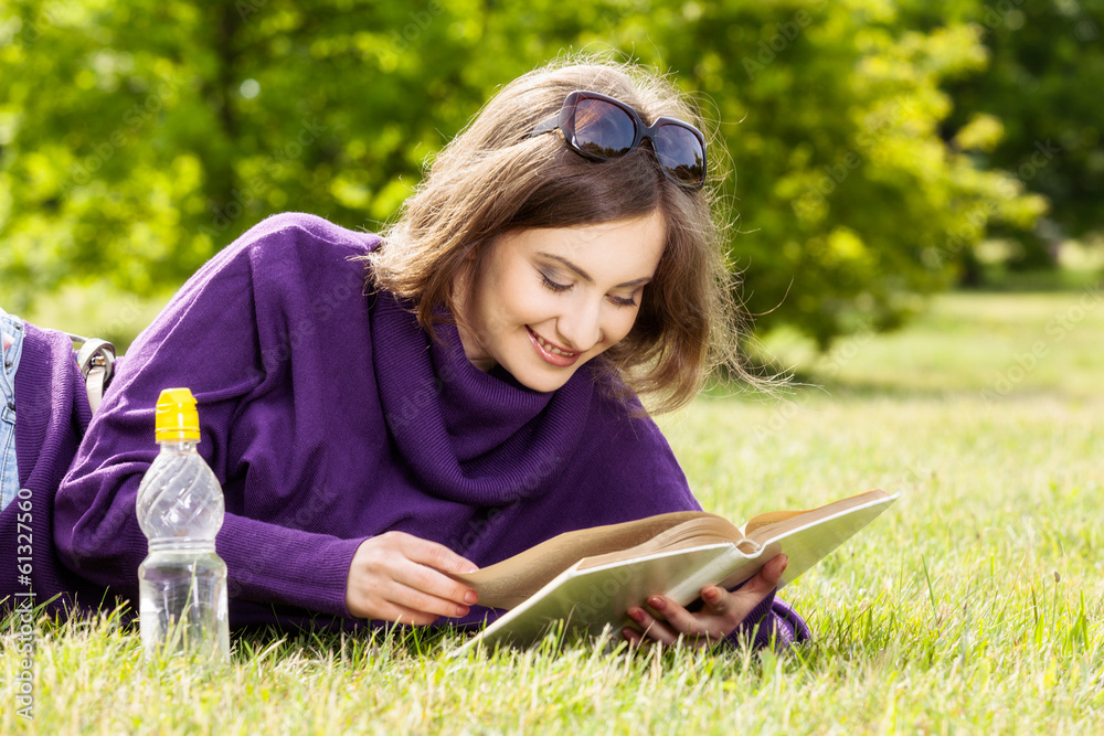 Happy woman reading book lying down on grass Happy woman reading book lying down on grass