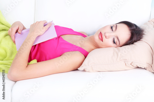 Beautiful young woman sleeping with book on sofa close up