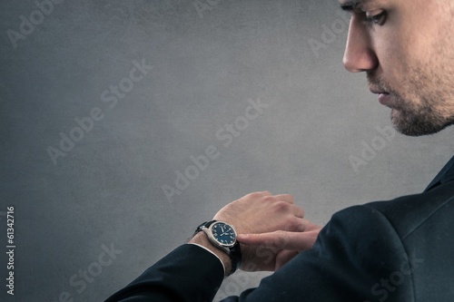 Businessman looking at the time on his wrist watch against dark photo