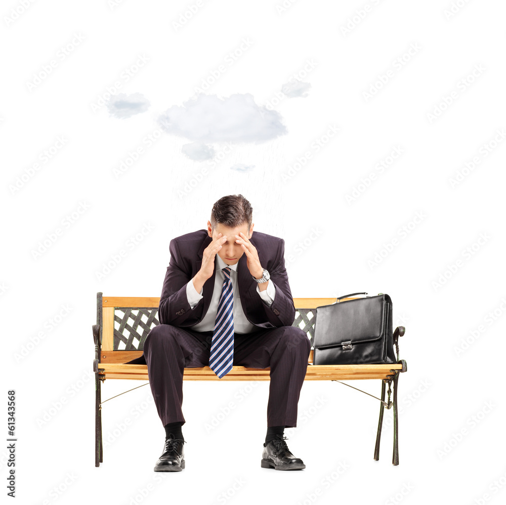 Worried young businessman sitting on bench with cloud over head