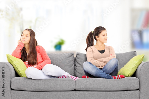 Two angry teenage girls sitting on sofa, at home,