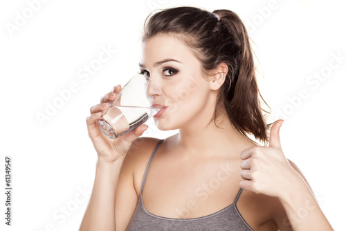 Fotografering beautiful woman drinks water from a glass and showing thumbs up