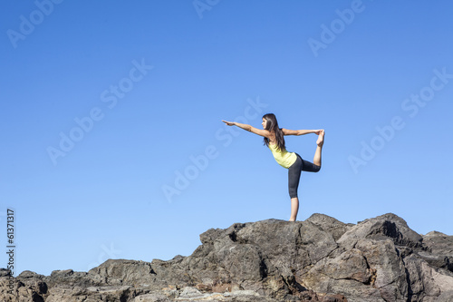 Young attractive woman doing dancers yoga pose on rocks against