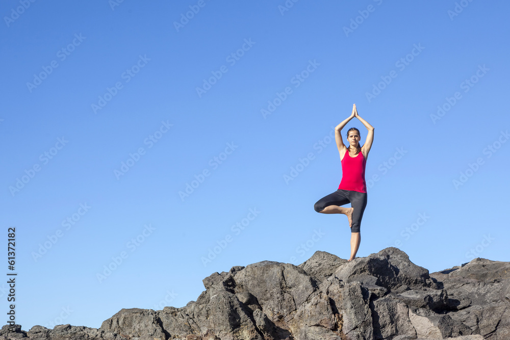 Young woman practicing tree yoga pose outdoor against blue sky