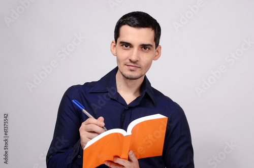 Student holding a book smiling. Teacher writing on a notebook.