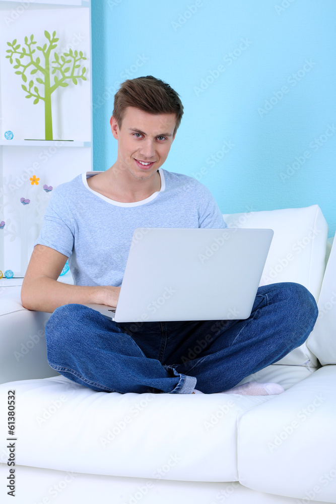 Guy sitting on sofa with laptop on blue background