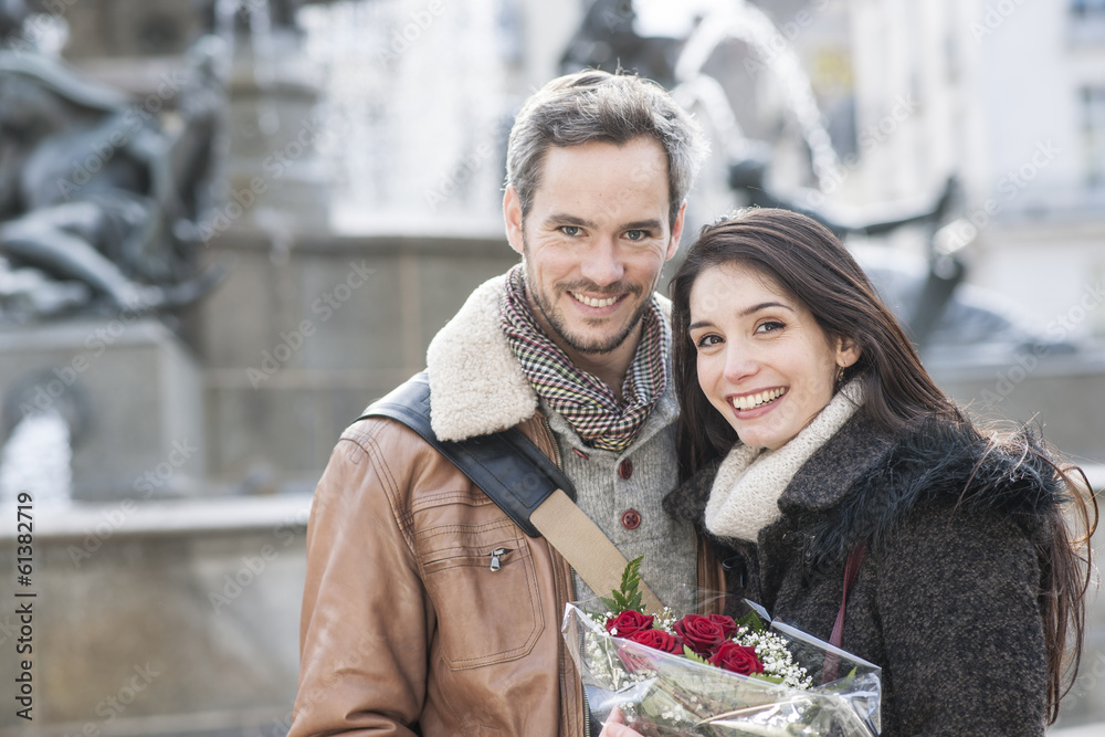 Obraz premium romantic couple with flowers bouquet with fountain in background