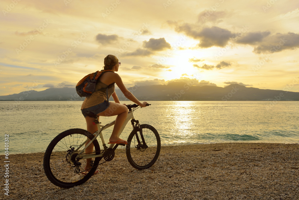 Obraz premium Young woman with backpack standing on the shore near his bike an