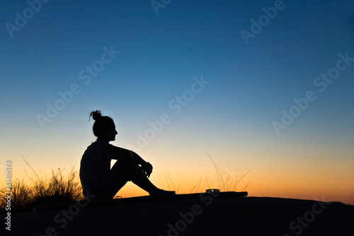 Silhouette de femme assise  soleil couchant