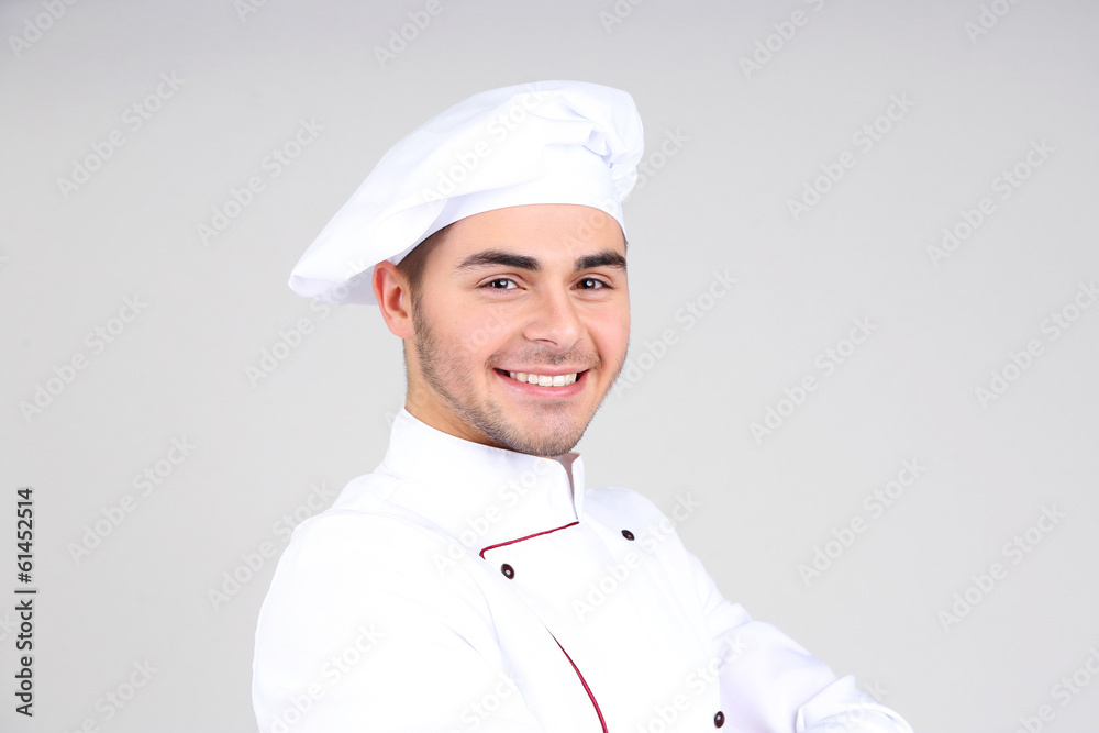 Professional chef in white uniform and hat, on gray background