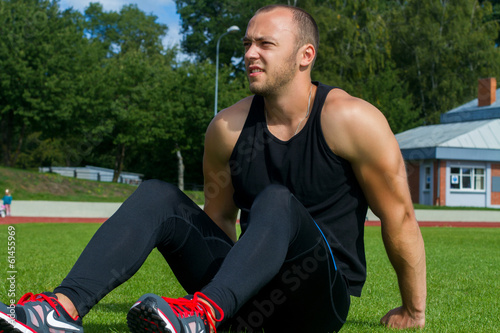 Fototapeta Naklejka Na Ścianę i Meble -  Image of muscle man sitting on stadium grass