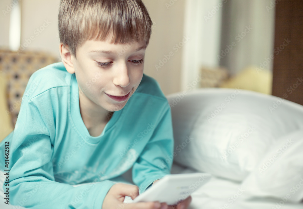 Beautiful child lying on a bed playing at computer toy smiling Beautiful child lying on a bed playing at computer toy smiling