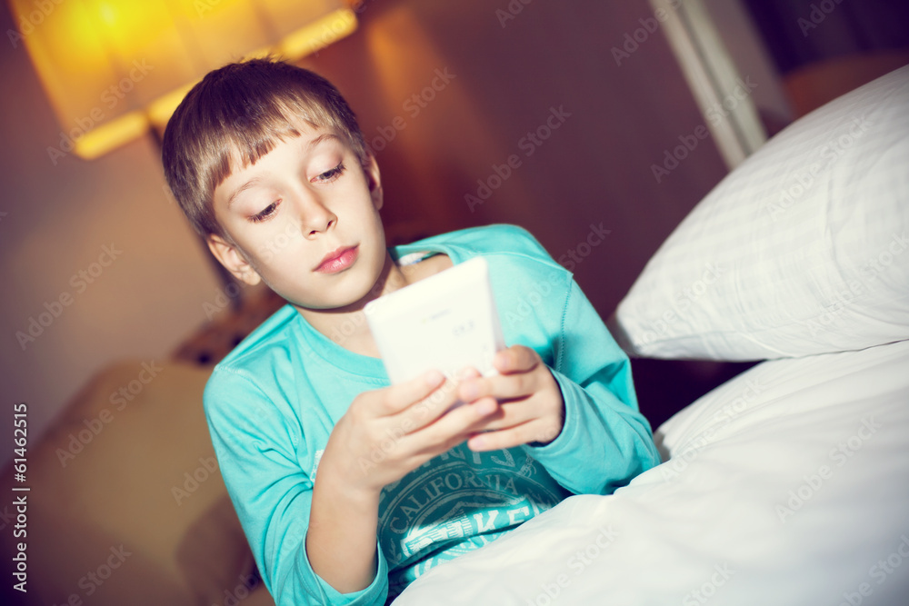 Beautiful blond child playing tablet pc lying on bed Beautiful blond child playing tablet pc lying on bed