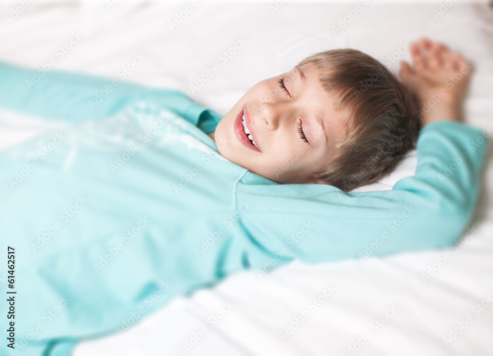 Lovely little boy peacefully sleeping in a bed smiling