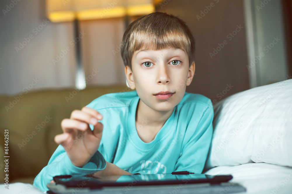 Beautiful child lying on a cozy bed playing at tablet computer Beautiful child lying on a cozy bed playing at tablet computer