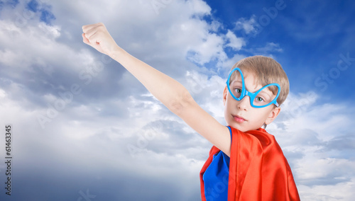 Cute little child dressed as superhero against blue sky