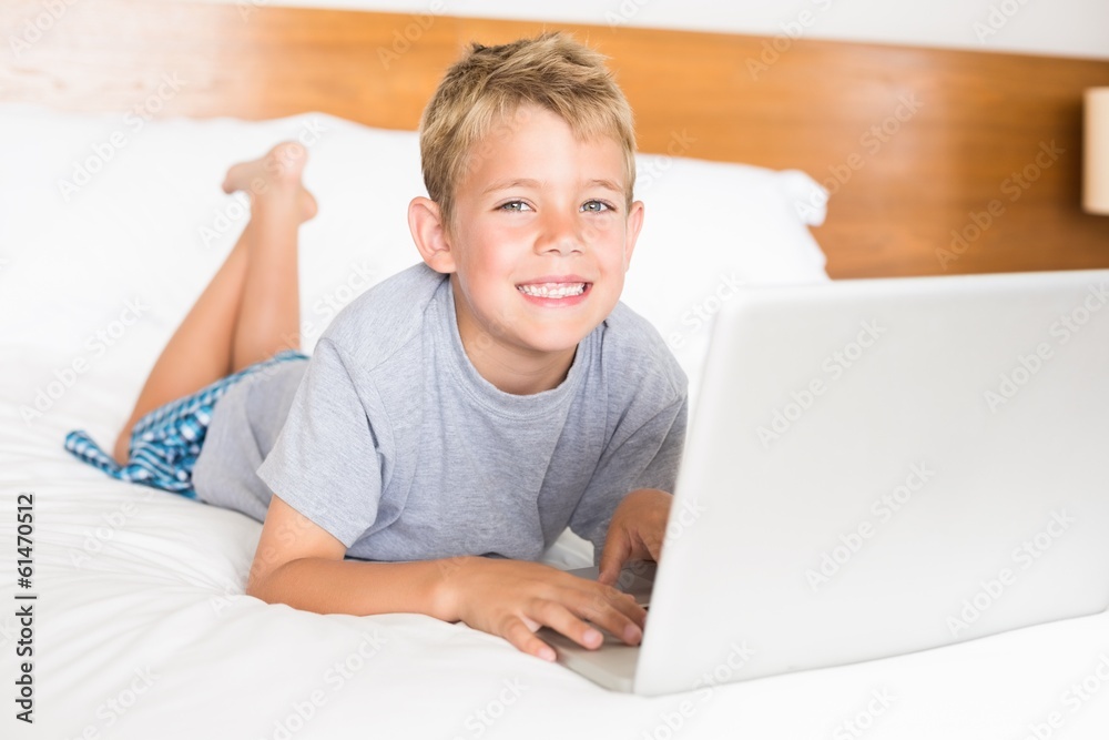 Happy blonde boy lying on bed using laptop Happy blonde boy lying on bed using laptop