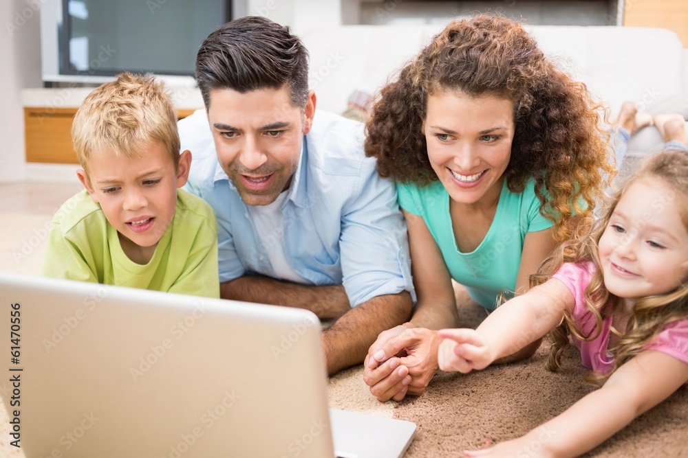 Cute siblings lying on the rug using laptop with their parents Cute siblings lying on the rug using laptop with their parents