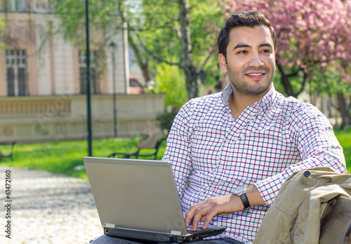 Happy man sitting on bench and using laptop