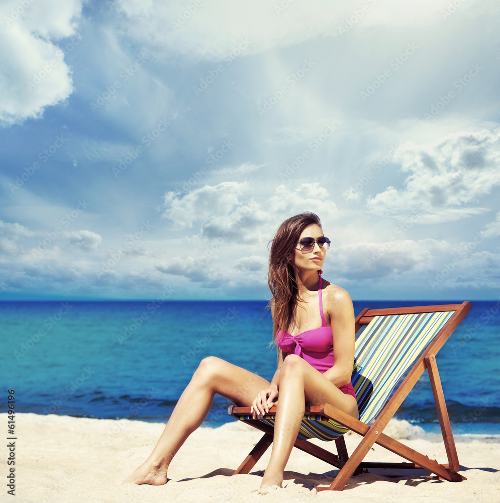 A young woman in a swimsuit relaxing on a deckchair on the beach A young woman in a swimsuit relaxing on a deckchair on the beach