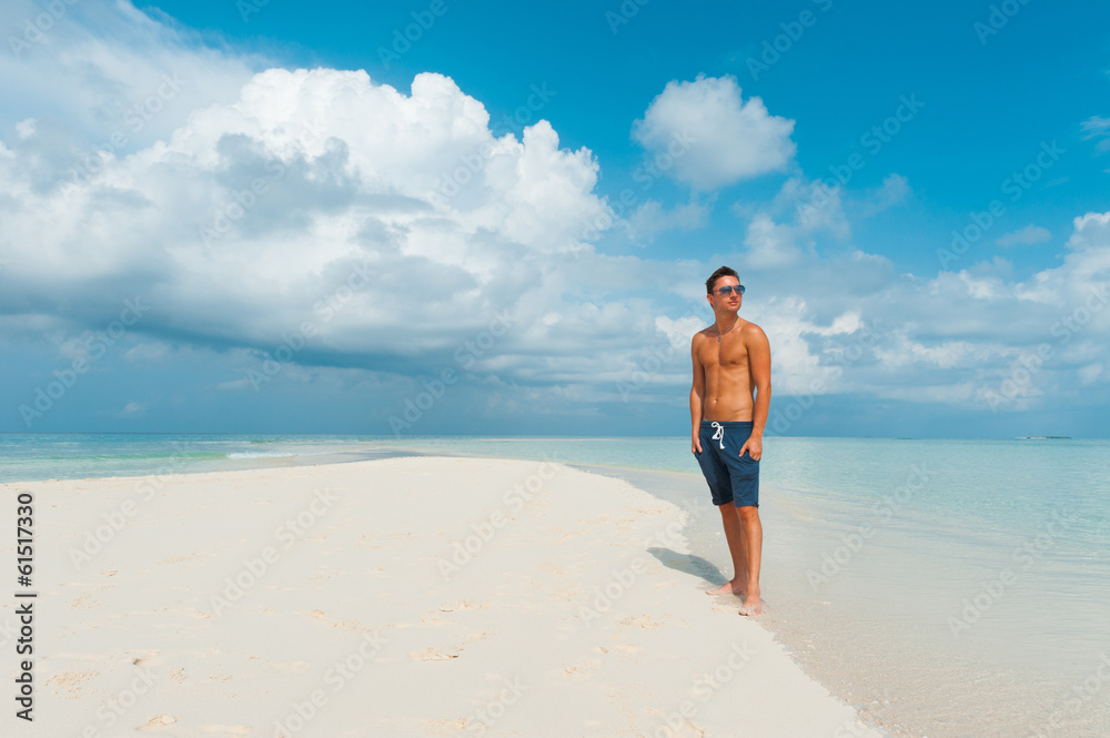Attractive male looks around standing on beautiful beach with wh Attractive male looks around standing on beautiful beach with wh