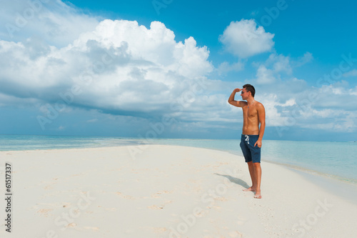 Attractive young male looks away standing on beautiful beach wit