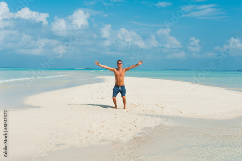 Happy attractive young male jumps on beach with white sand and o