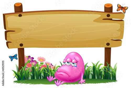 A pink beanie monster under the empty wooden signboard