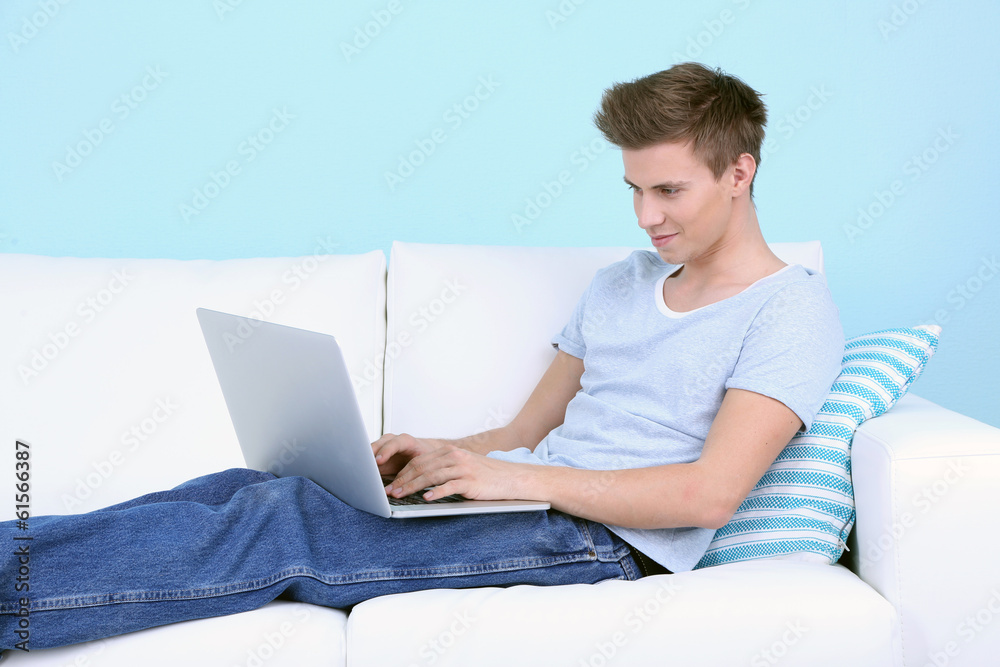 Guy lie on sofa with laptop on blue background Guy lie on sofa with laptop on blue background