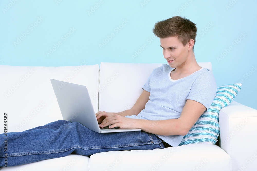 Guy lie on sofa with laptop on blue background