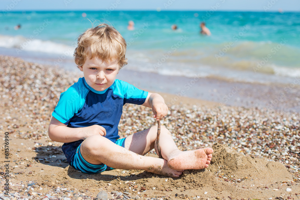 Little toddler boy playing with sand and stones on the beach Little toddler boy playing with sand and stones on the beach
