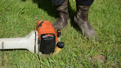 Gardener man in gumboots hand start gass trimmer cutter photo