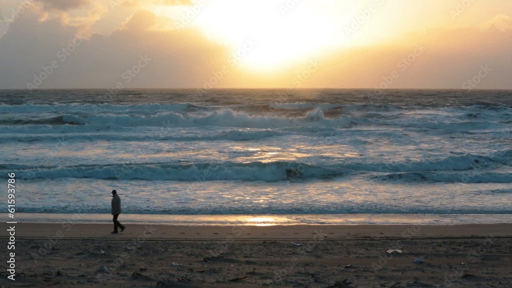 Man walking on the beach with storm waves at sunset Man walking on the beach with storm waves at sunset