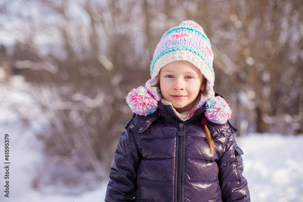 Portrait of a little adorable girl in winter hat in snowy forest