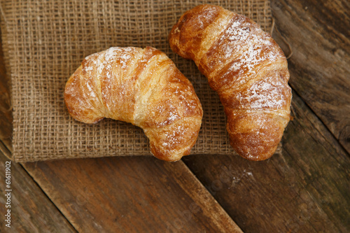 Two sugar powder croissants on a wooden suface