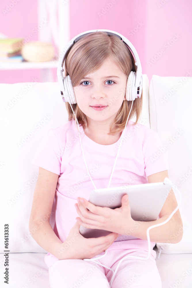 Naklejka premium Little girl sitting on sofa and listening music in room