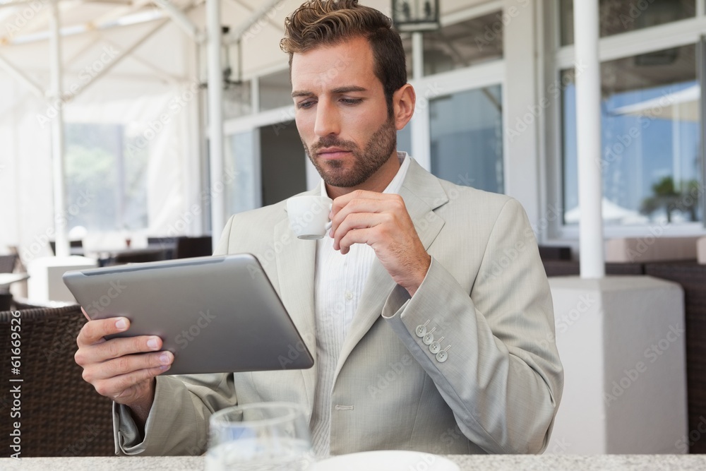 Fototapeta premium Handsome young businessman working on tablet drinking espresso