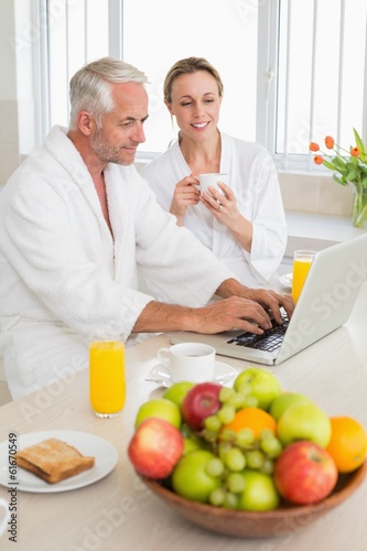 Smiling couple using laptop at breakfast in bathrobes