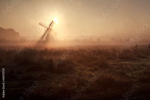sunshine behind windmill in misty morning