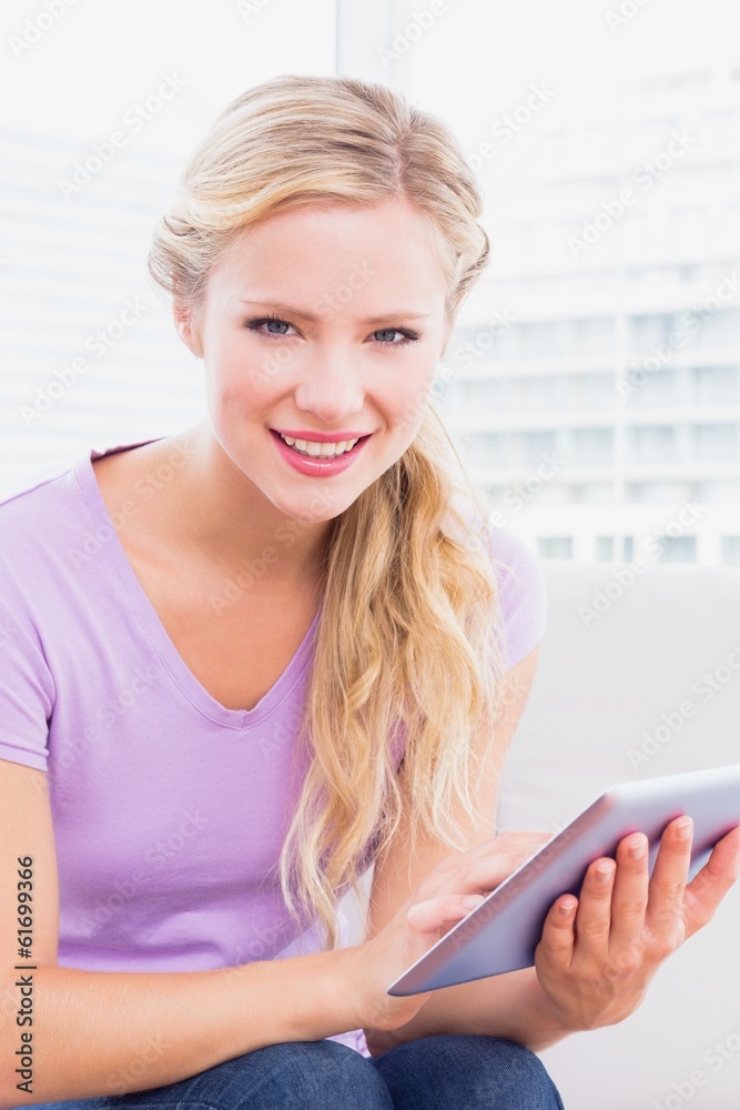Smiling blonde sitting on her sofa using her tablet pc Smiling blonde sitting on her sofa using her tablet pc