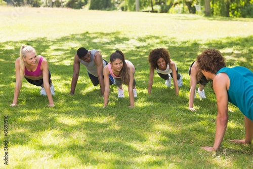 Instructor with fitness class doing push ups in park