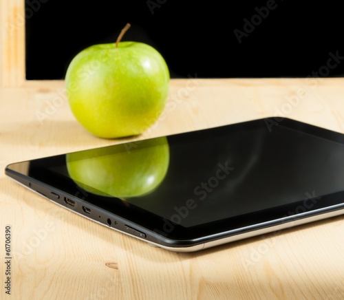 tablet pc and green apple in front of blackboard on wood table