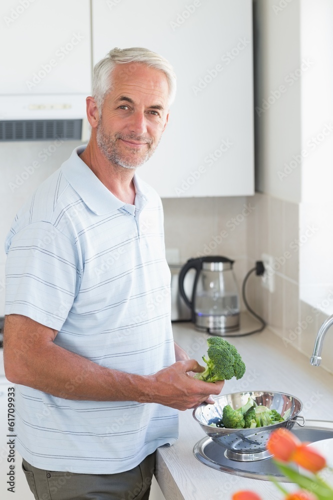 Casual man rinsing broccoli in colander and smiling at camera Casual man rinsing broccoli in colander and smiling at camera
