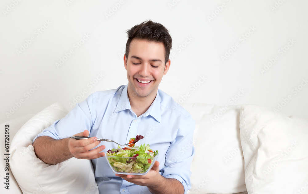 Junger Mann auf dem Sofa freut sich über seinen Salat