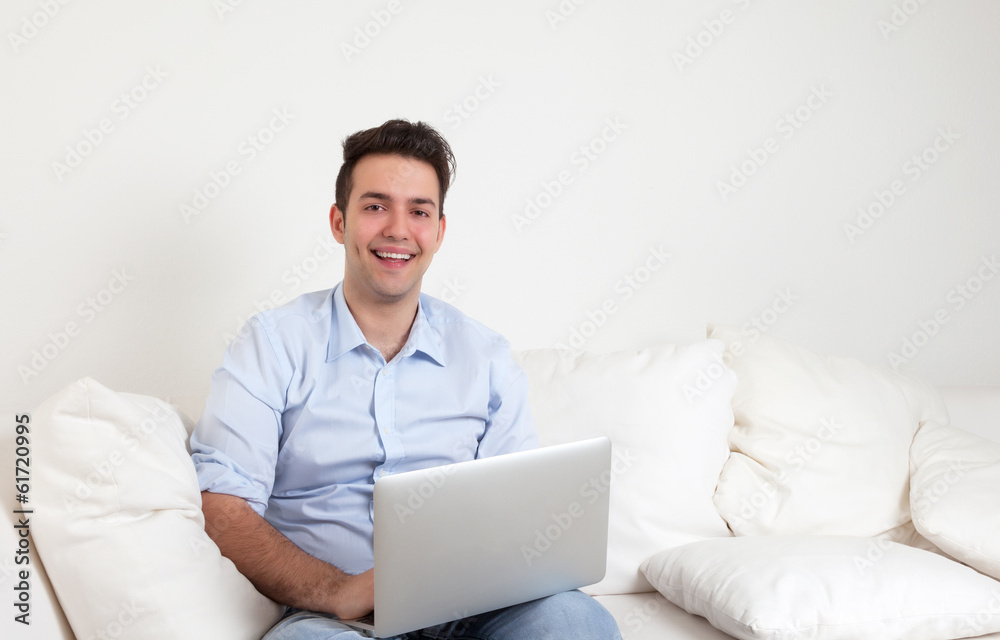 Lachender junger Mann mit Notebook auf dem Sofa Lachender junger Mann mit Notebook auf dem Sofa