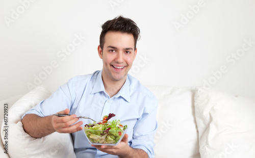 Junger Mann isst frischen Salat auf dem Sofa