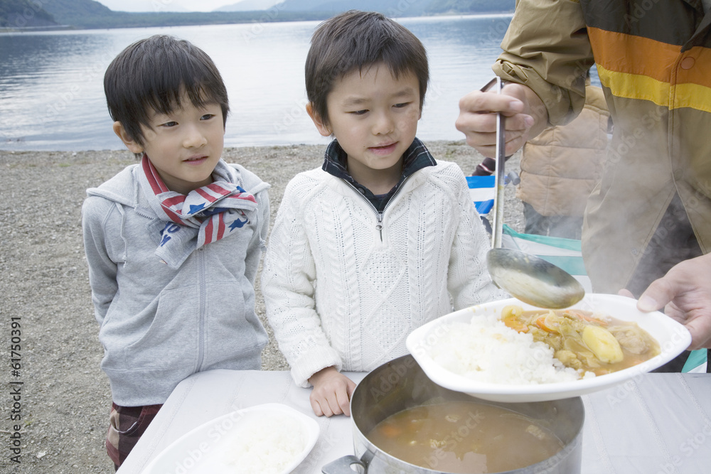 Two boys served curry by lakeside