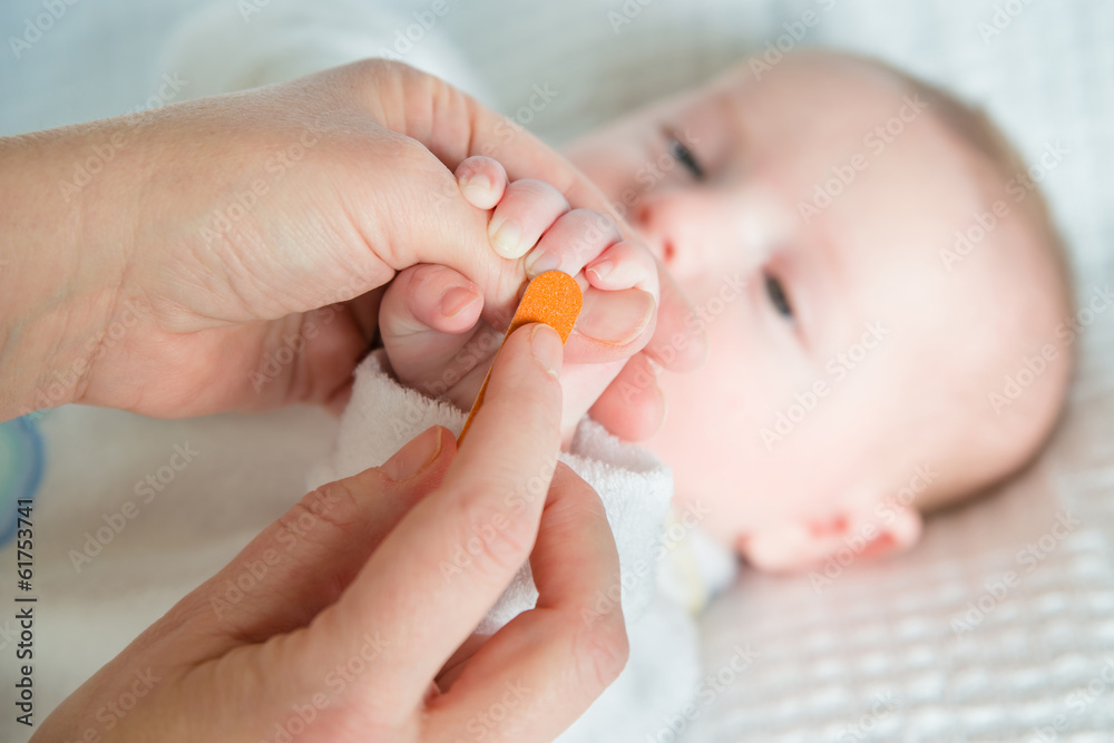 Mother filing and smoothing baby's fingernails with nail file